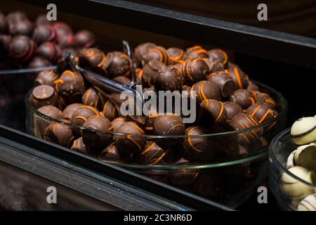 Selektiver Fokus, Nahaufnahme belgischer Pralinen in der Schüssel, Edelstahlzange Stockfoto