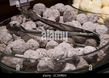 Selektiver Fokus, Nahaufnahme belgischer Pralinen in der Schüssel, bedeckt mit weißem Schropfpulver und Edelstahlzange. Stockfoto