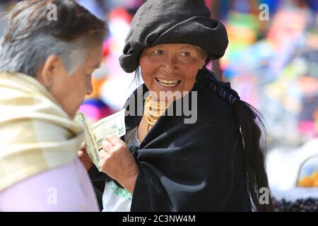 Ältere indigene Frau lächelt, während sie einen Haufen US-Dollar-Scheine auf dem Otavalo-Markt in Ecuador zählt. Stockfoto