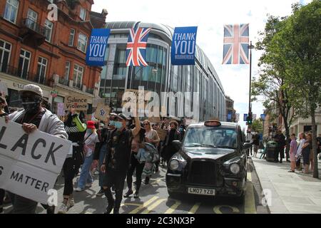 Protestierende mit Banner marschieren an einem schwarzen Londoner Taxi vorbei. Londoner nahmen an einem friedlichen Protest der Black Lives Matter im Hyde Park Teil, bevor sie zur Downing Street marschierten. Die Demonstration ist eine von vielen auf der ganzen Welt nach dem Tod von George Floyd, während in der Obhut von Minneapolis. Stockfoto