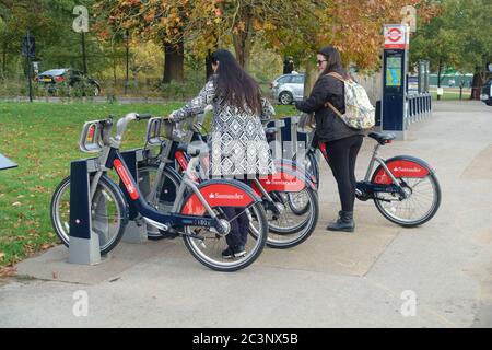 Zwei Frauen im Fahrradständer mit Santander Leihfahrrädern im Hyde Park, London, Großbritannien Stockfoto