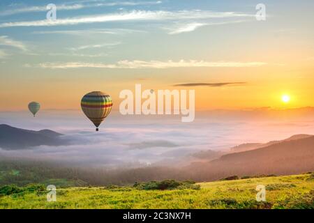 Große Heißluft-Baloons über idyllische Landschaft mit grünen Gras bedeckt Morgen Berge mit fernen Gipfeln und breiten Tal voller dicken weißen wolkigen fo Stockfoto