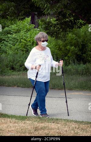 Eine Frau mittleren Alters, die mit Gehstöcken und einer chirurgischen Maske unterwegs ist, um eine Übungswanderung zu machen. In Little Bay Park, Whitestone, Queens, New York City. Stockfoto