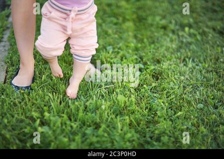 Mutter lehrt ihr Baby, die ersten Schritte barfuß auf dem Gras zu machen. Stockfoto