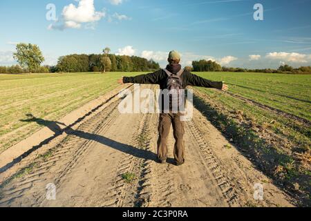Ein Mann mit Rucksack auf einer unbefestigten Straße, Blick in sonnigen Tag Stockfoto
