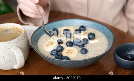 Gesunde Frühstückschale mit Haferbrei Haferbrei mit Heidelbeeren und Bananenscheiben. Frau essen gesundes Frühstück Stockfoto