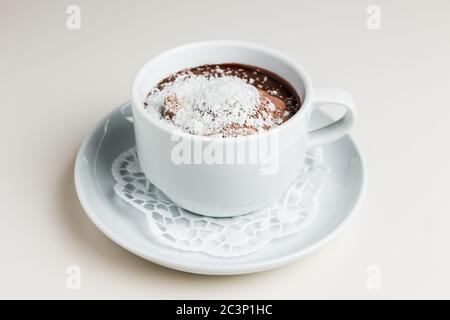 Eine kleine weiße Tasse dunkle heiße Schokolade mit Schokoladeneis und Kokosflocken auf einer weißen Untertasse und einer Serviette Stockfoto