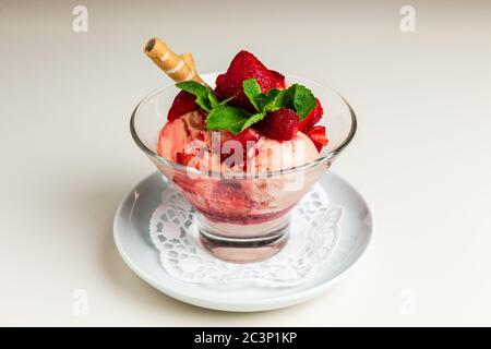 Erdbeereis mit frischen Erdbeeren, garniert mit einer Waffel und Minze, serviert in einer transparenten Glasschüssel Stockfoto