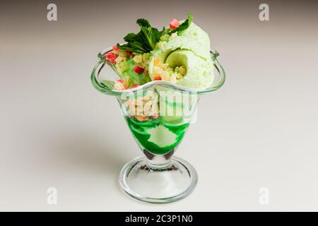 Pistazien-Eis mit kandierten Früchten und grünem Sirup, garniert mit Minze, serviert in einer transparenten Glasvase Stockfoto