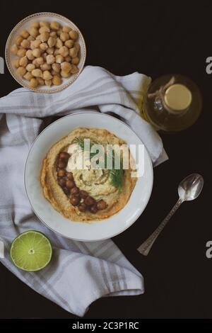 Kichererbsen veganen Hummus garniert mit Dill und gebackenen Kichererbsen auf schwarzem Hintergrund mit Vintage Löffel, Flasche Olivenöl, Handtuch, Kichererbsen Stockfoto