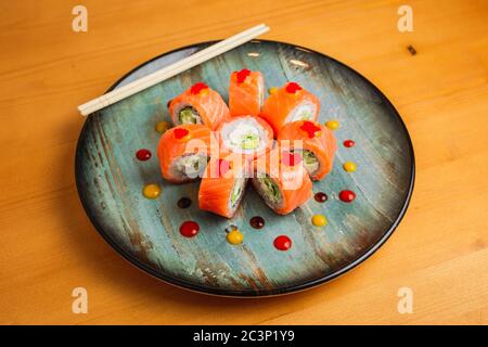 Brötchen mit Lachs, Gurke und Frischkäse, verziert mit fliegendem Fischkaviar, serviert auf einem blauen Teller Stockfoto
