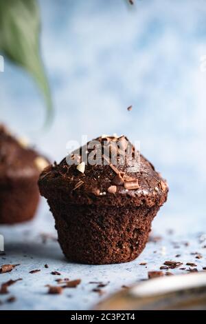 Vertikale selektive Fokusaufnahme von Schokolade Cupcakes auf einem blauen Oberfläche mit Schokolade Chips fallen Stockfoto