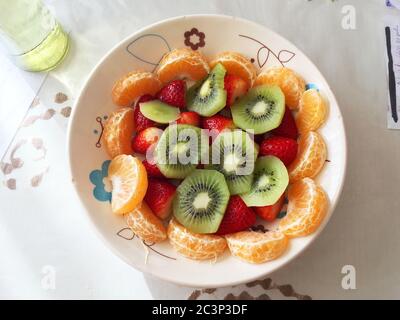 Nahaufnahme von köstlichen Obstsalat mit Kiwi, Erdbeeren und Mandarine auf einem Teller Stockfoto