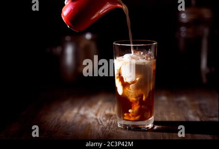 Eiskaffee in einem hohen Glas mit übergossenem Sahne, Eiswürfeln und Bohnen auf einem alten rustikalen Holztisch. Stockfoto