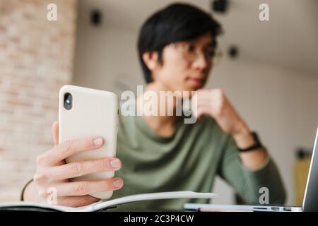 Bild von schönen jungen asiatischen Mann trägt Brillen mit Laptop und Handy in der Wohnung Stockfoto