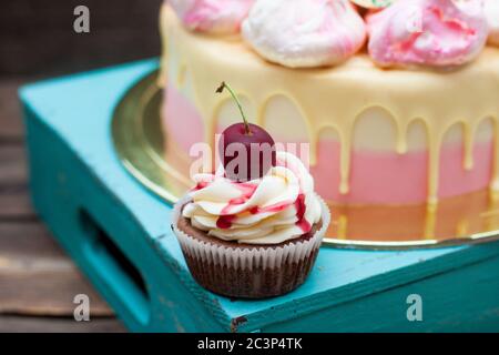 Schokoladenkuchen mit Beerensauce, Schlagsahne und frischer Kirsche darauf. Rosa Kuchen auf dem Hintergrund. Stockfoto