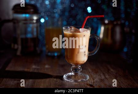 Eiskaffee in einem Latte-Glas mit übergossenem Sahne, Eiswürfeln und Bohnen auf einem alten rustikalen Holztisch. Auf einem dunkelblauen Bokeh-Hintergrund mit Kopierfläche. Stockfoto
