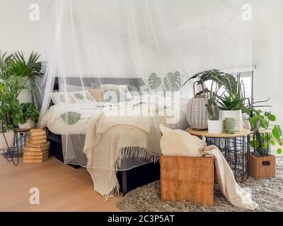 Helles weißes Schlafzimmer mit zahlreichen Zimmerpflanzen und Tageslicht Stockfoto