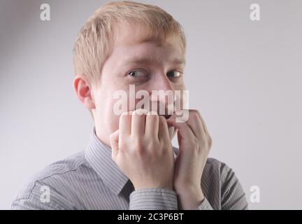 Ansicht eines Mannes, der beim Beißen ein graues Hemd trägt Seine Nägel mit einem aufgeregten Gesichtsausdruck Stockfoto