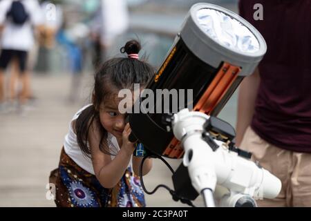 Hongkong, China. Juni 2020. Ein Kind beobachtet am 21. Juni 2020 eine ringförmige partielle Sonnenfinsternis mit Teleskop entlang einer Promenade in Hongkong. Eine partielle Sonnenfinsternis tritt auf, wenn ein Teil der Erde von dem Schatten (Penumbra), der vom Mond geworfen wird, umschlungen wird, während er zwischen unserem Planeten und der Sonne in unvollkommener Ausrichtung passiert. Während dieser ringförmigen Finsternis Ã das erste der Dekade Ã scheint der Mond die Sonne zu bedecken, so dass der Sonnenhalo als sichtbarer Rand einen Ringus bildet, im Volksmund bekannt als der 'Feuerring Credit: May James/ZUMA Wire/Alamy Live News Stockfoto