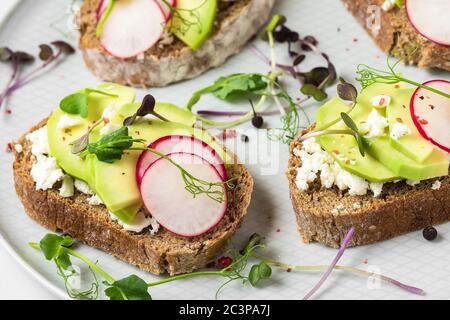 Gesunde Frühlings-Avocado-Toasts mit Rettich, Quark, Erbsensprossen und Pfeffer für eine gesunde Ernährung Frühstück. Close up Stockfoto
