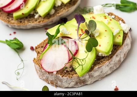 Avocado-Toasts mit Rettich, Feta-Käse, Sprossen und Pfeffer zum Frühstück auf weißem Marmortisch. Gesunde Ernährung Snacks. Close up Stockfoto