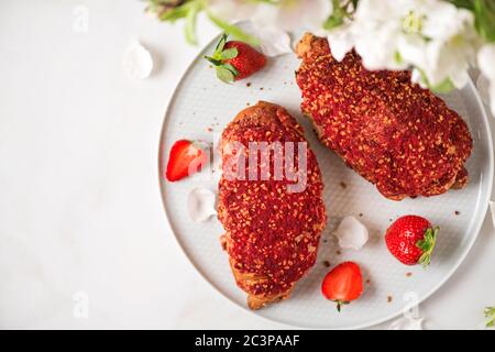 Croissants mit Beerenmarmelade und frischen Erdbeeren auf einem Teller und Blüten auf weißem Marmor Hintergrund. Draufsicht. Romantisches Frühstück. Weicher Fokus Stockfoto