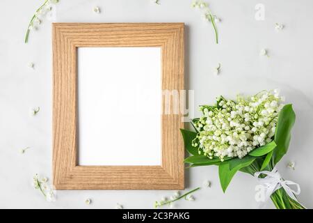 Blank Fotorahmen mit Maiglöckchen Blumenstrauß auf weißem Hintergrund. Mock up. Flach liegend. Draufsicht. Hochzeit oder festliches Konzept Stockfoto
