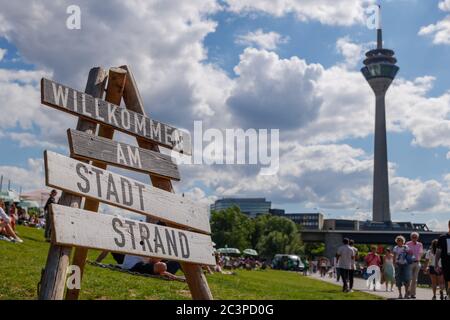 Holzschild mit ' Willkommen AM Stat Strand' bedeutet Willkommen in City's Beach Side, und verschwommen Hintergrund Menschen hängen entlang der Flussseite des Rheins. Stockfoto