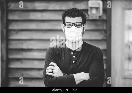 Graustufenaufnahme eines Mannes, der eine Brille und eine Sanitäranlage trägt Gesichtsmaske vor einer Holzwand Stockfoto