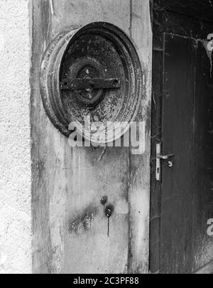 Vertikale Graustufenaufnahme eines Metallreifen-Rings auf dem Wand durch die Holztür eines verlassenen Hauses Stockfoto