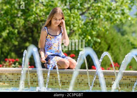 Ein Mädchen sitzt am Brunnen und schaut auf die Wasserstrahlen Stockfoto