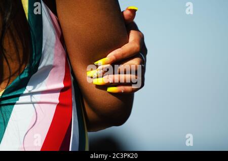 Nahaufnahme von knallbunten langen Fingernägeln auf einer unerkennbaren jungen Frau in einem bunten Badeanzug am Strand Stockfoto