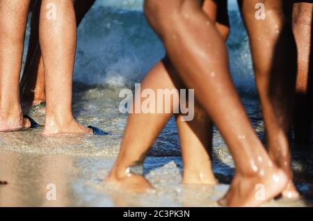 Nahaufnahme der Beine von unerkennbaren jungen Menschen, die den Strand in goldenem Sonnenlicht genießen Stockfoto