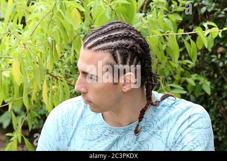 Attraktives, kaukasisches männliches Modell mit Zöpfen, die im Freien in der Natur posieren. Stil, Trends, Modekonzept. Stockfoto