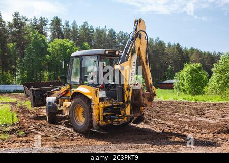 Clearing und Nivellierung eines privaten Grundstücks. Gelbe Bagger angetriebene Erde in einem breiten Eimer, Rückansicht Stockfoto