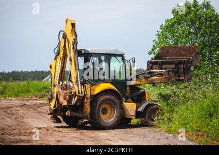 Gelber Bagger lädt Ladung auf dem Gras. Lichtung Land von Bäumen, Rasen und Schutt Stockfoto