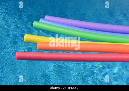 Regenbogenfarbene Poolnudeln schwimmen an einem hellen und sonnigen Tag in einem Schwimmbad. Stockfoto