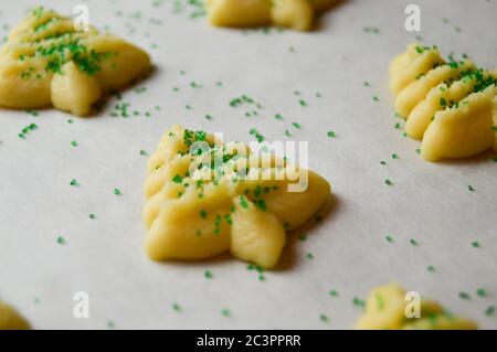 spritz Kekse in weihnachtsbaumformen auf Pergamentpapier mit grünen Zuckerstreuseln Stockfoto