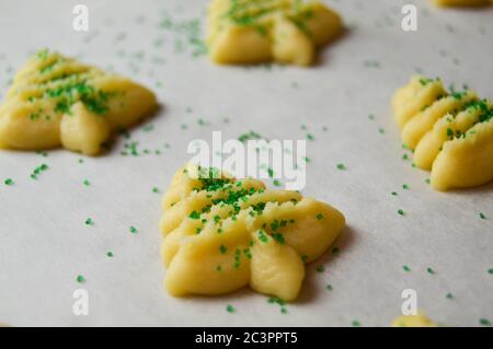 spritz Kekse in weihnachtsbaumformen auf Pergamentpapier mit grünen Zuckerstreuseln Stockfoto