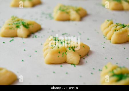 spritz Kekse in weihnachtsbaumformen auf Pergamentpapier mit grünen Zuckerstreuseln Stockfoto