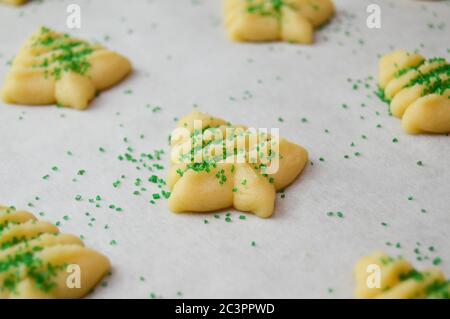 spritz Kekse in weihnachtsbaumformen auf Pergamentpapier mit grünen Zuckerstreuseln Stockfoto