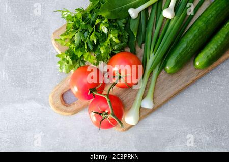 Holzschneidebrett mit frischem Gemüse auf Stein Beton Tisch. Draufsicht Tomaten, Gurken, Zwiebeln, Petersilie. Frisches gesundes Essen Konzept. Stockfoto