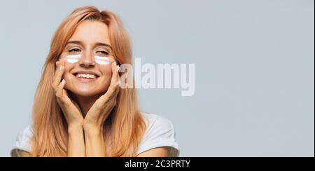 Portrait der jungen fröhlichen niedlichen Frau lächeln und Anwendung Sonnencreme (Sonnencreme) auf das Gesicht. Hübsches weibliches verschmiertes Gesicht, Wangen mit Sonnenschutz Stockfoto