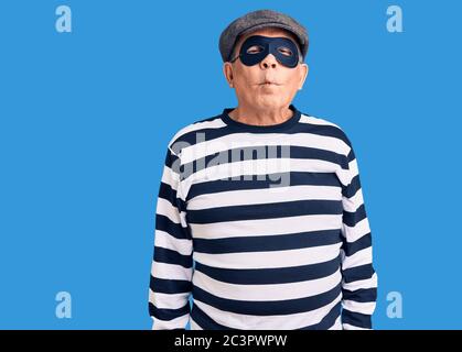 Senior stattlichen Mann trägt Einbrecher Maske und T-Shirt machen Fisch Gesicht mit Lippen, verrückt und komisch Geste. Lustiger Ausdruck. Stockfoto