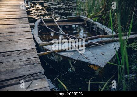 Nahaufnahme eines alten hölzernen Bootes, gefüllt mit Wasser daneben Eine Promenade an einem Sumpf Stockfoto