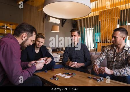 Mehrere Männer spielen Poker in einem Café und halten Karten in ihren Händen Stockfoto