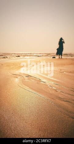 Silhouette einer jungen Frau, die allein auf einem Sand steht Strand Stockfoto