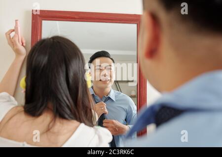 Junge asiatische Paar vor dem Spiegel stehen, wenn immer bereit in den Morgen. Mann binden Krawatte und Frau Anwendung Make-up Stockfoto