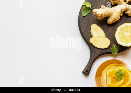 Blick von oben auf heißen Tee in Teekanne serviert in der Nähe Holzbrett mit Ingwerwurzel, Zitrone und Minze auf weißem Hintergrund Stockfoto